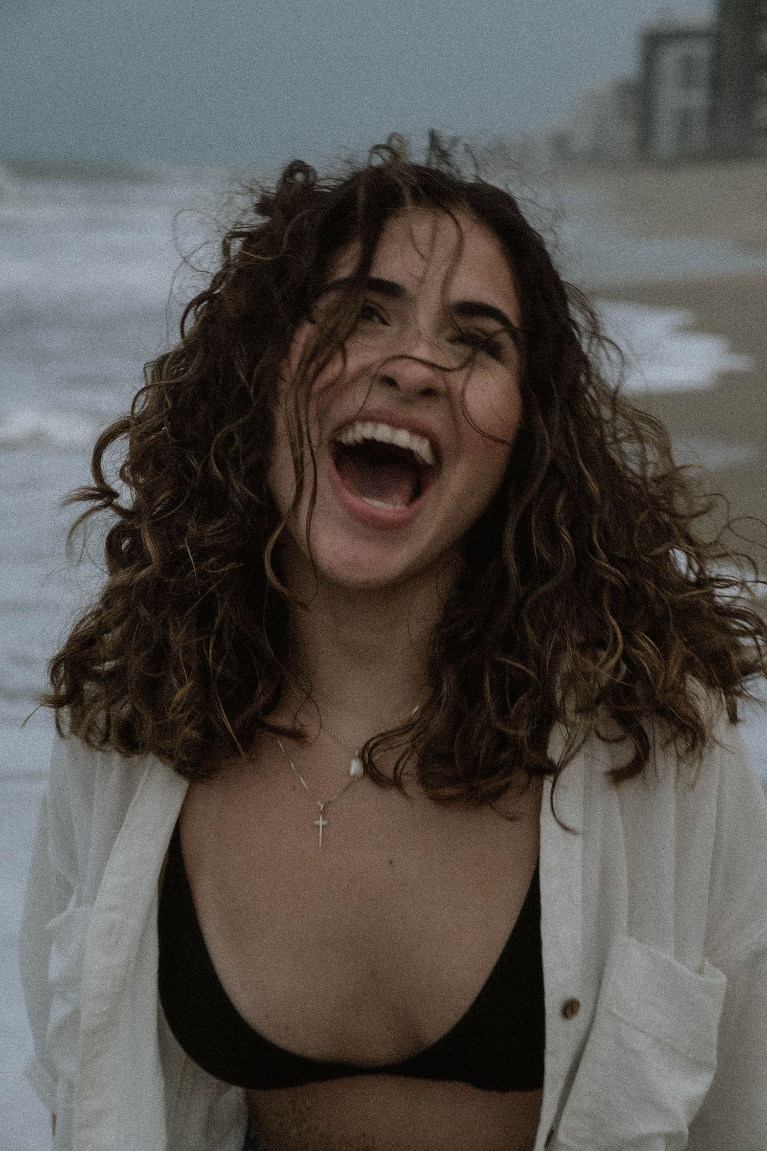 Candid laughing moment captured with curly hair and white shirt against moody backdrop.