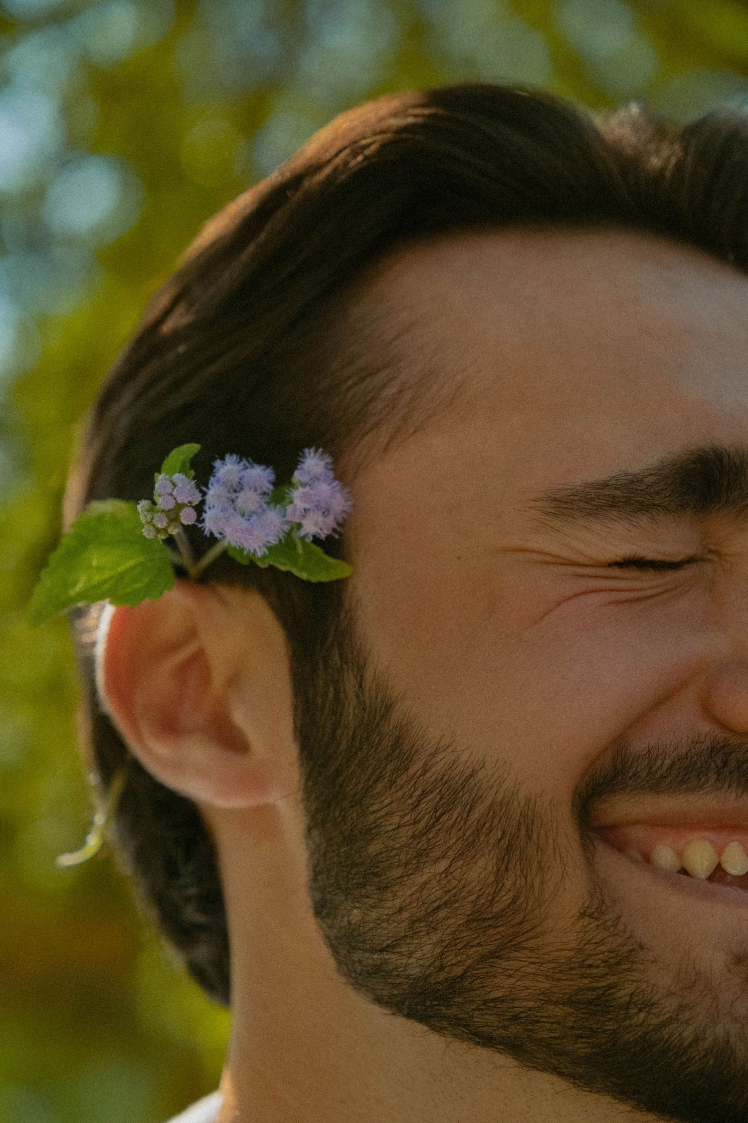 Close-up profile shots with delicate purple flowers in hair against natural backdrop.