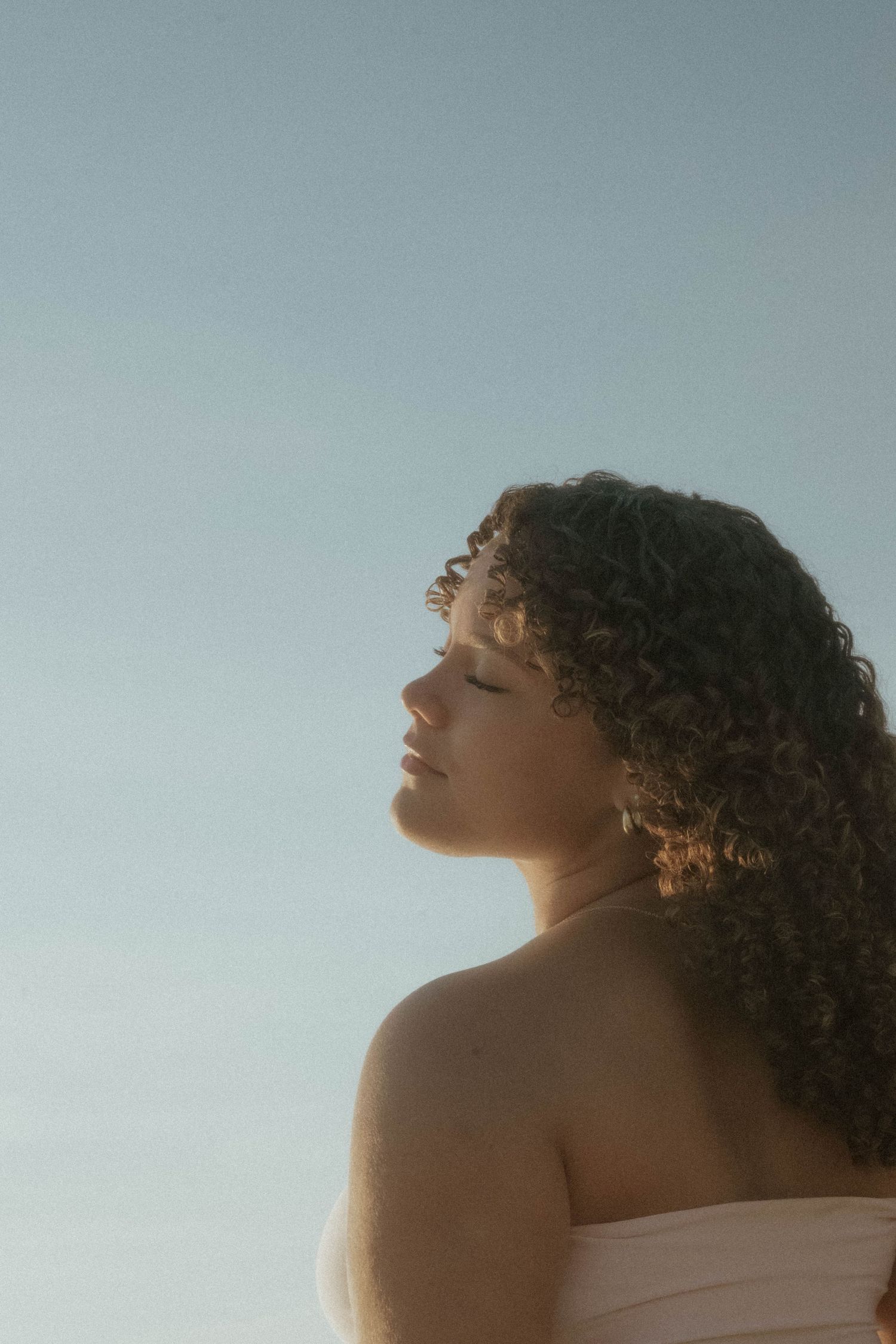 Silhouetted profile against soft sky showing curly hair in golden light.