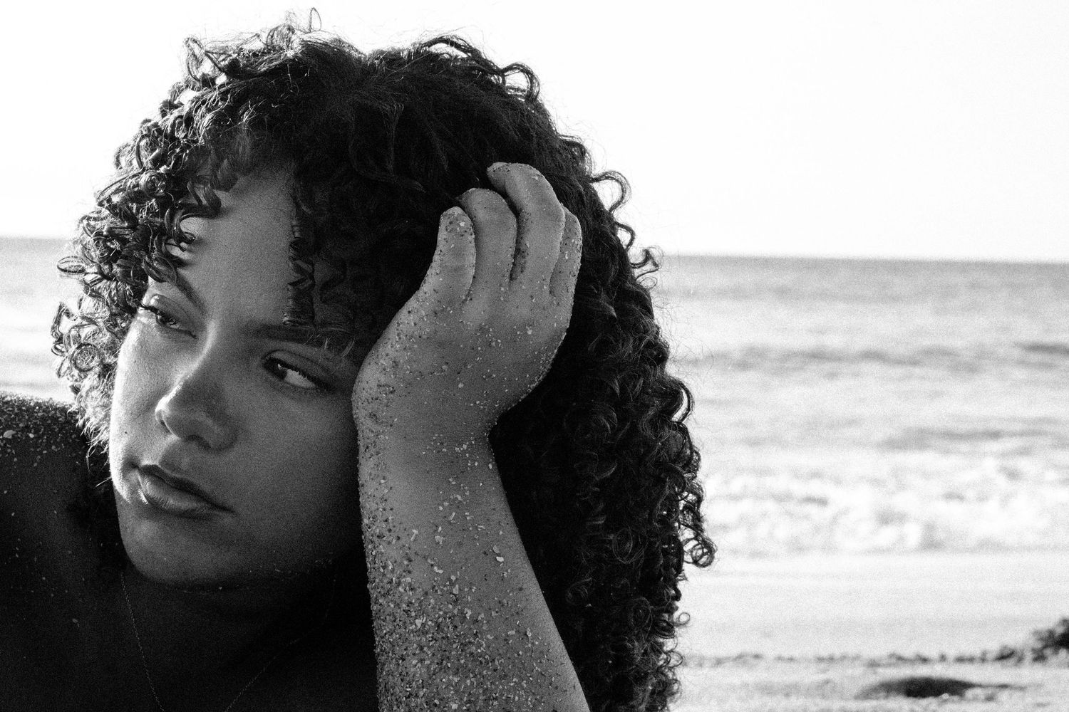 Black and white beach portrait with wind-swept curly hair.