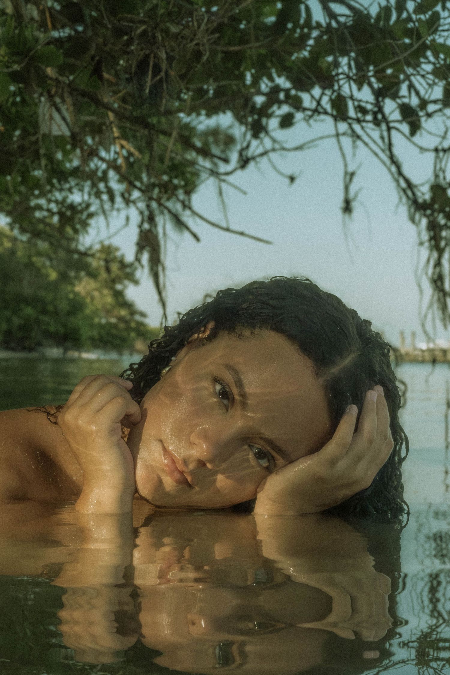 Artistic portrait reflected in still water with lush greenery overhead.