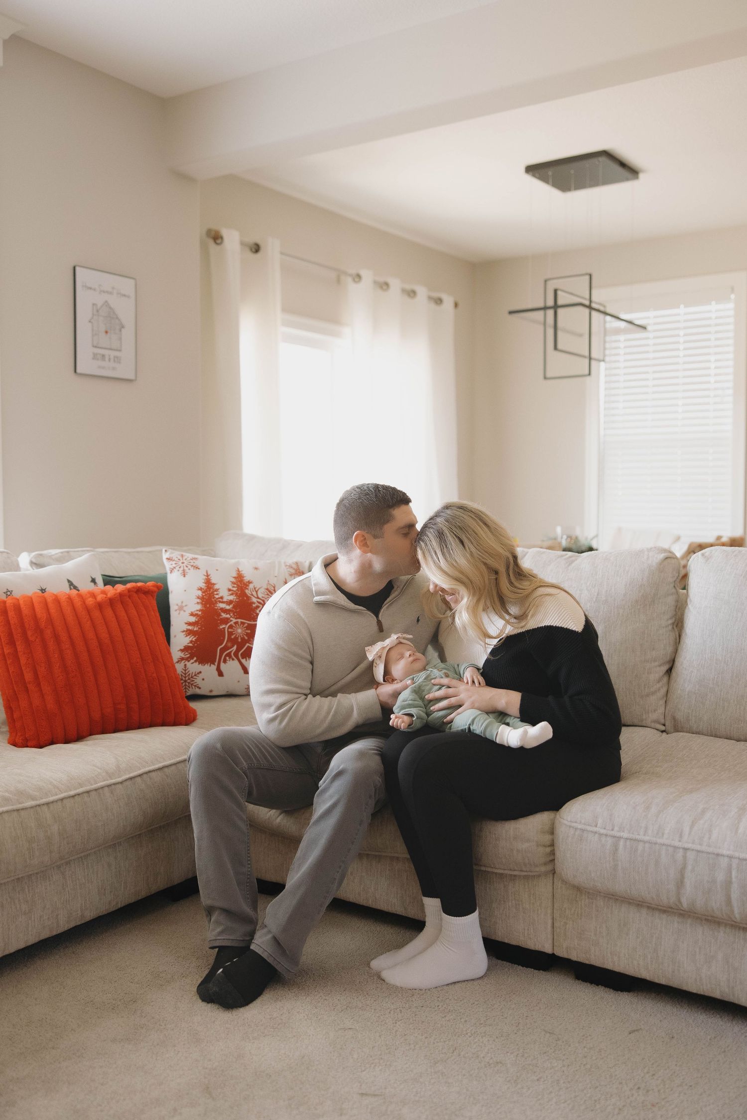 A tender family moment shared on a beige couch with orange accent pillows in a bright living room.