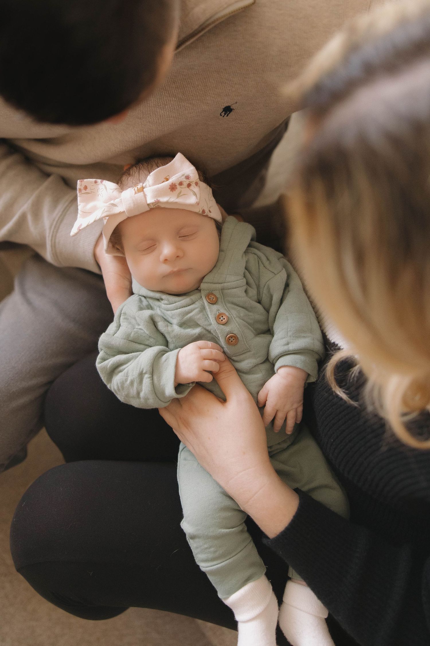 A tiny baby wearing a mint green outfit rests peacefully in someone's arms.