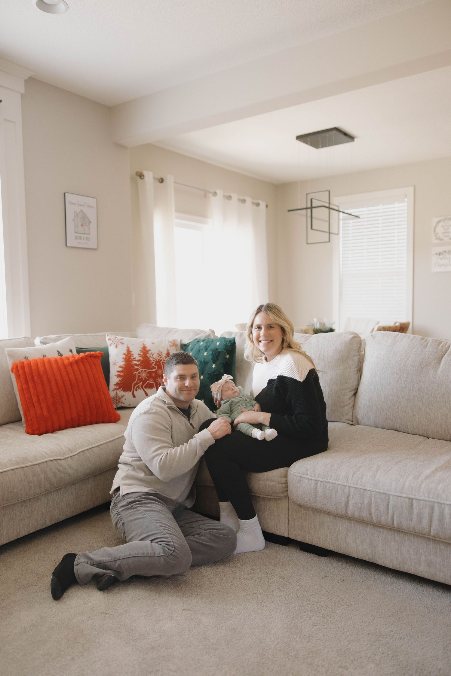 A person in gray lounges on a light-colored couch in a bright living room with decorative pillows.