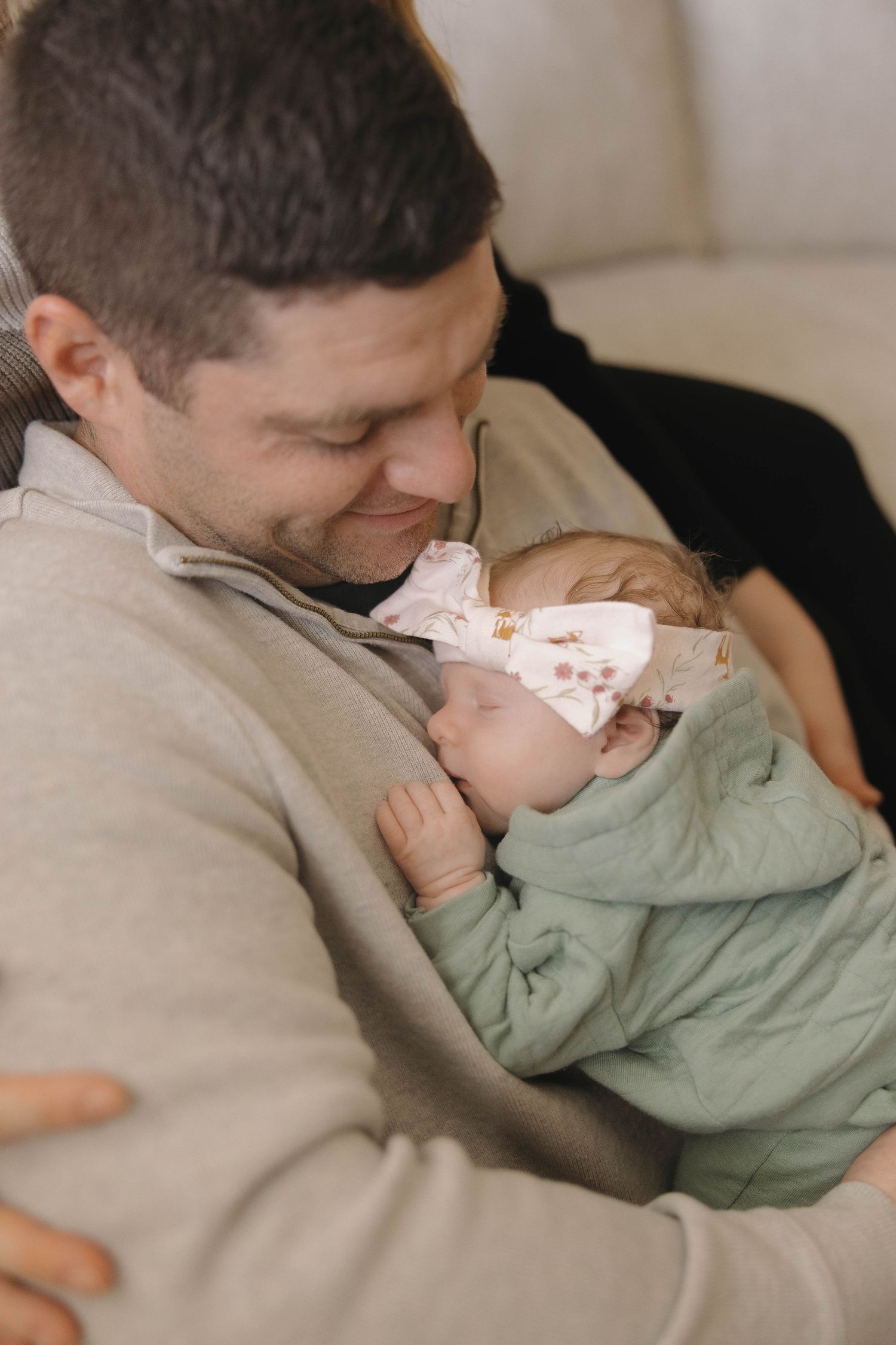 A tender moment between parent and infant cuddled together on a couch in soft natural lighting.