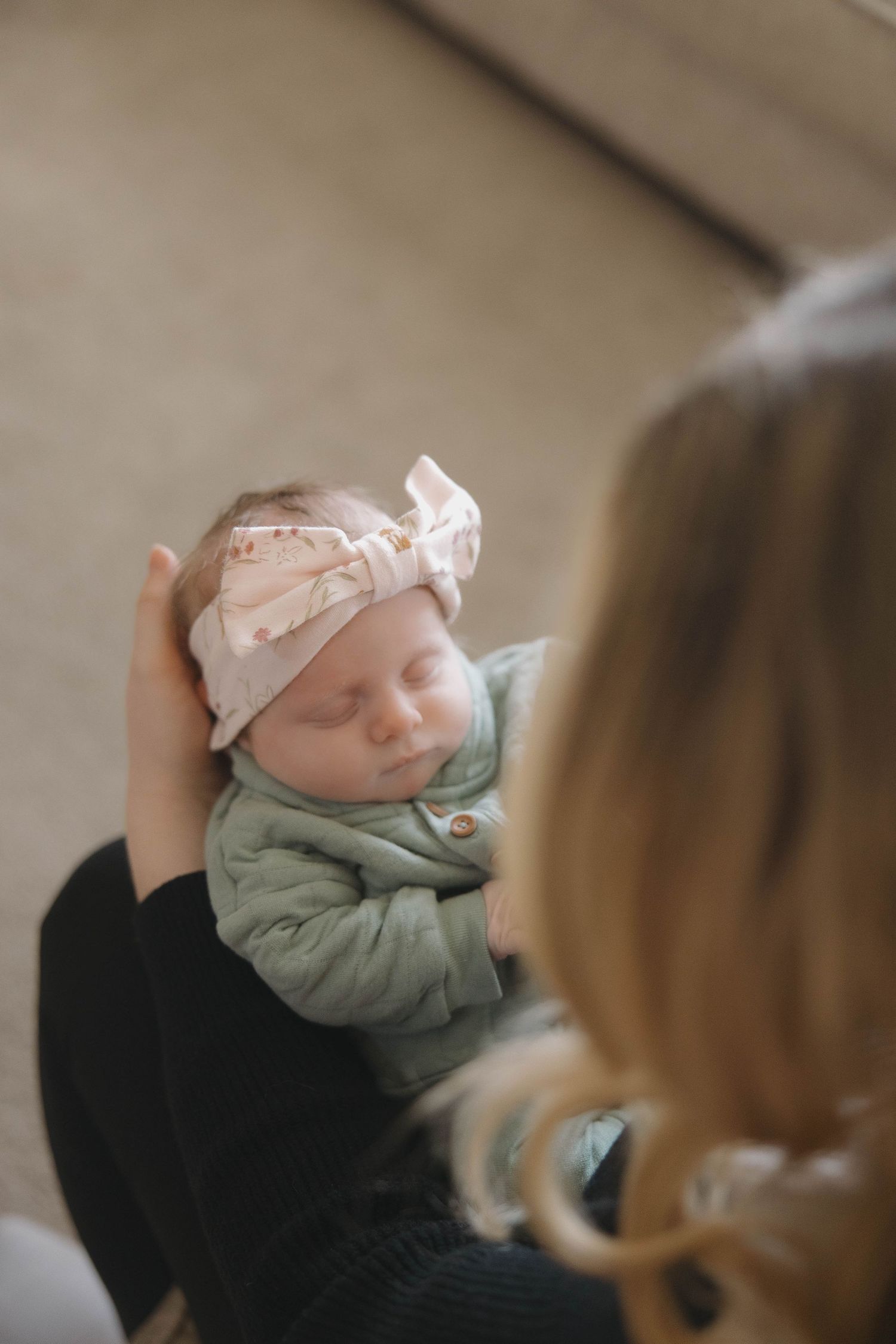 Close-up view of a sleeping newborn wearing a floral headband and mint green outfit being cradled.