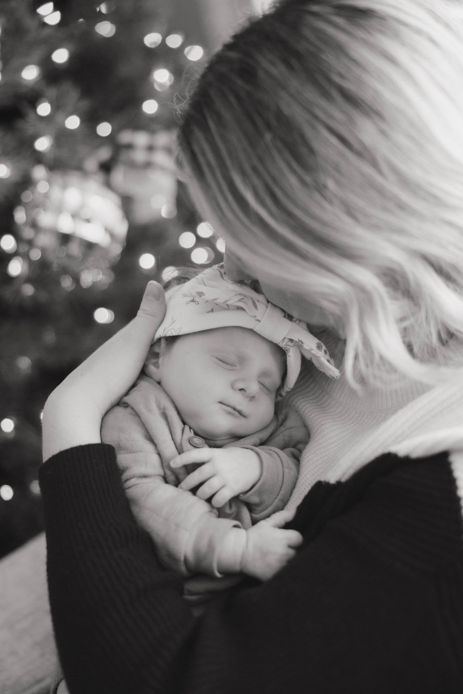 Black and white photo series of a sleeping baby being gently held against someone wearing black in a dimly lit setting.