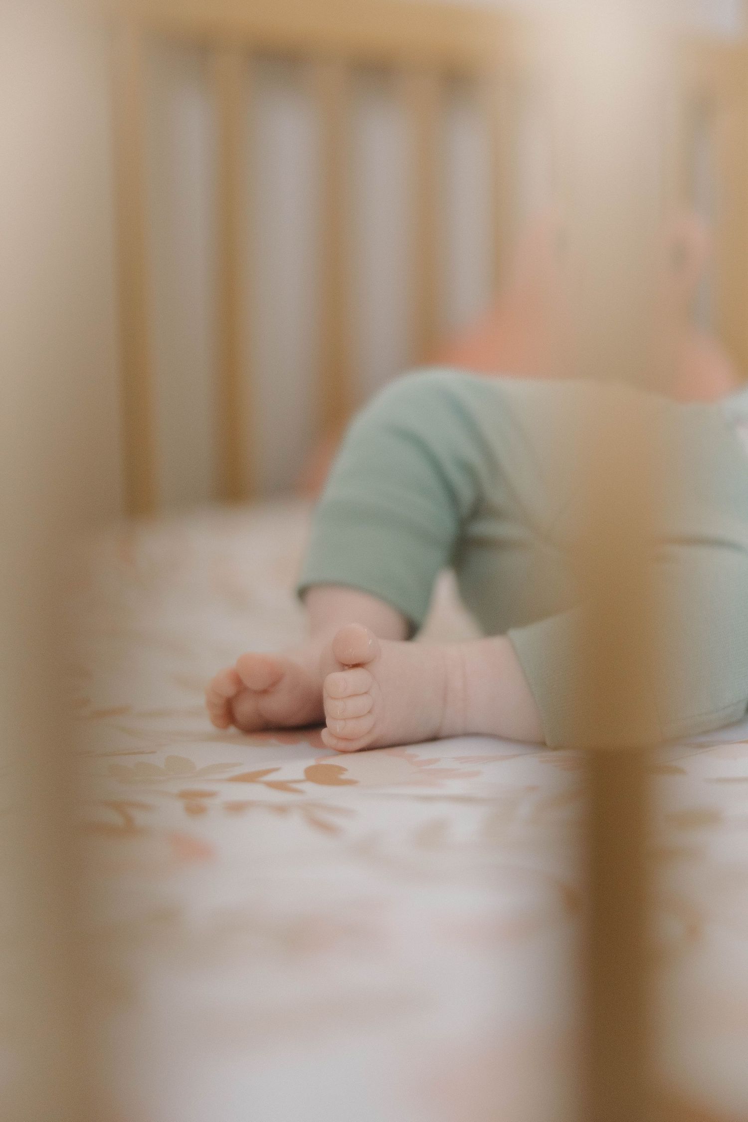 A tiny baby hand rests gently on soft white bedding inside a wooden crib.