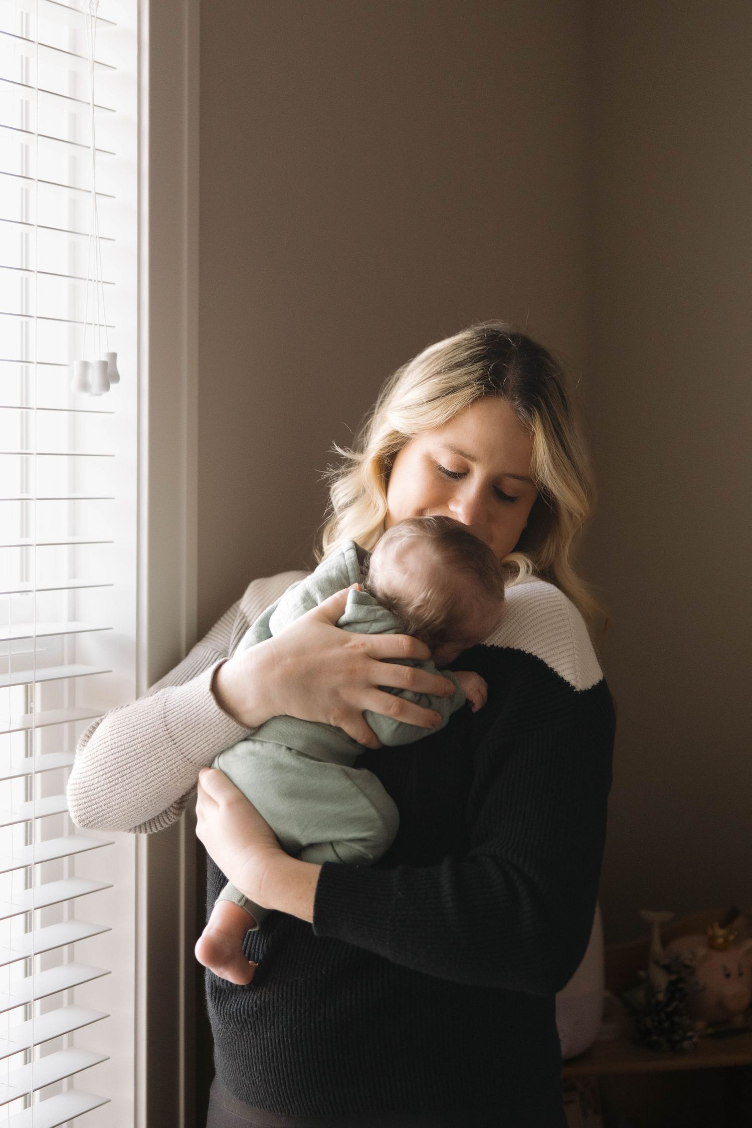 Intimate moment by a window as a parent embraces a sleeping infant wearing mint green.