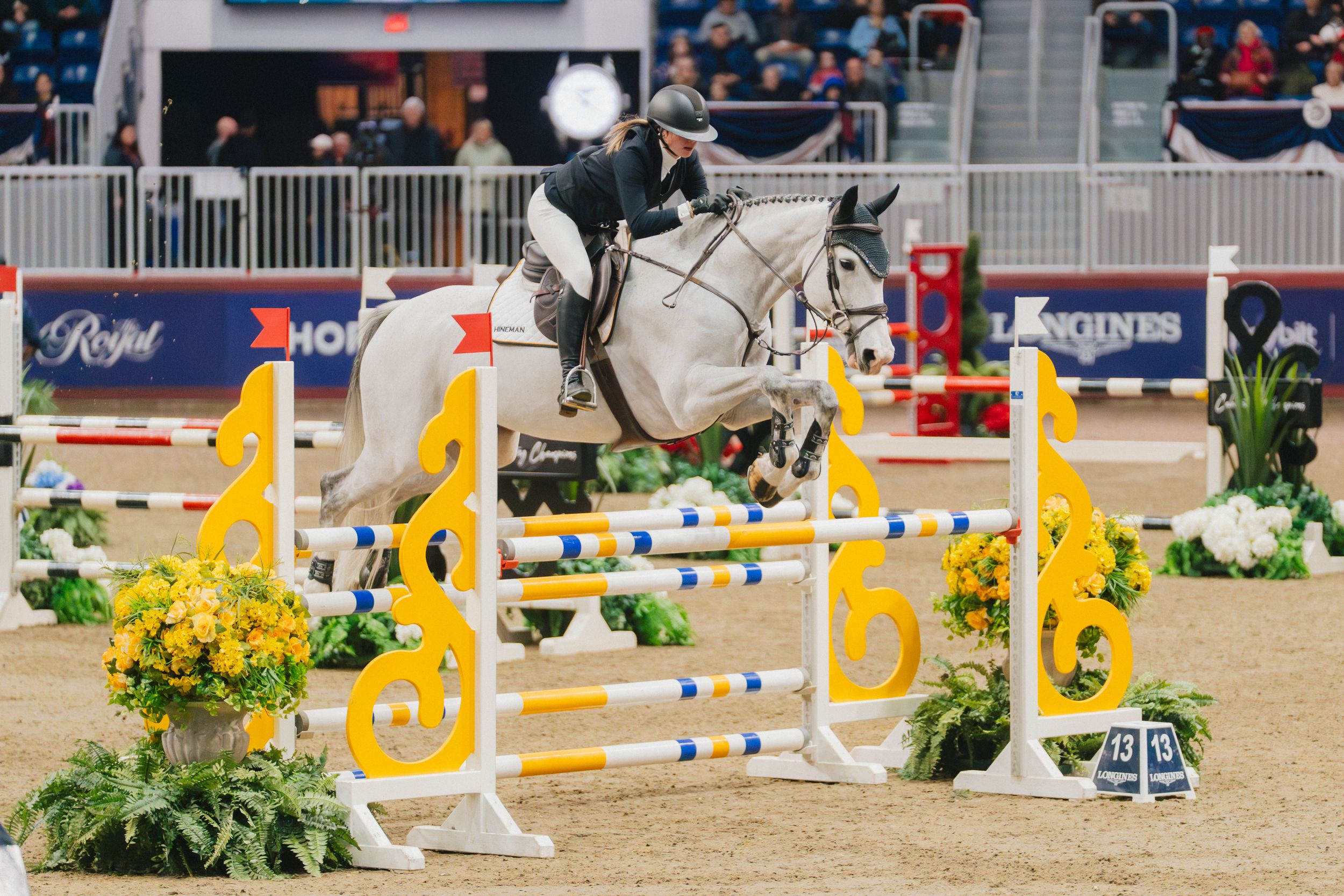 Horse and rider clearing a yellow and white striped jump rail during an equestrian show jumping competition.