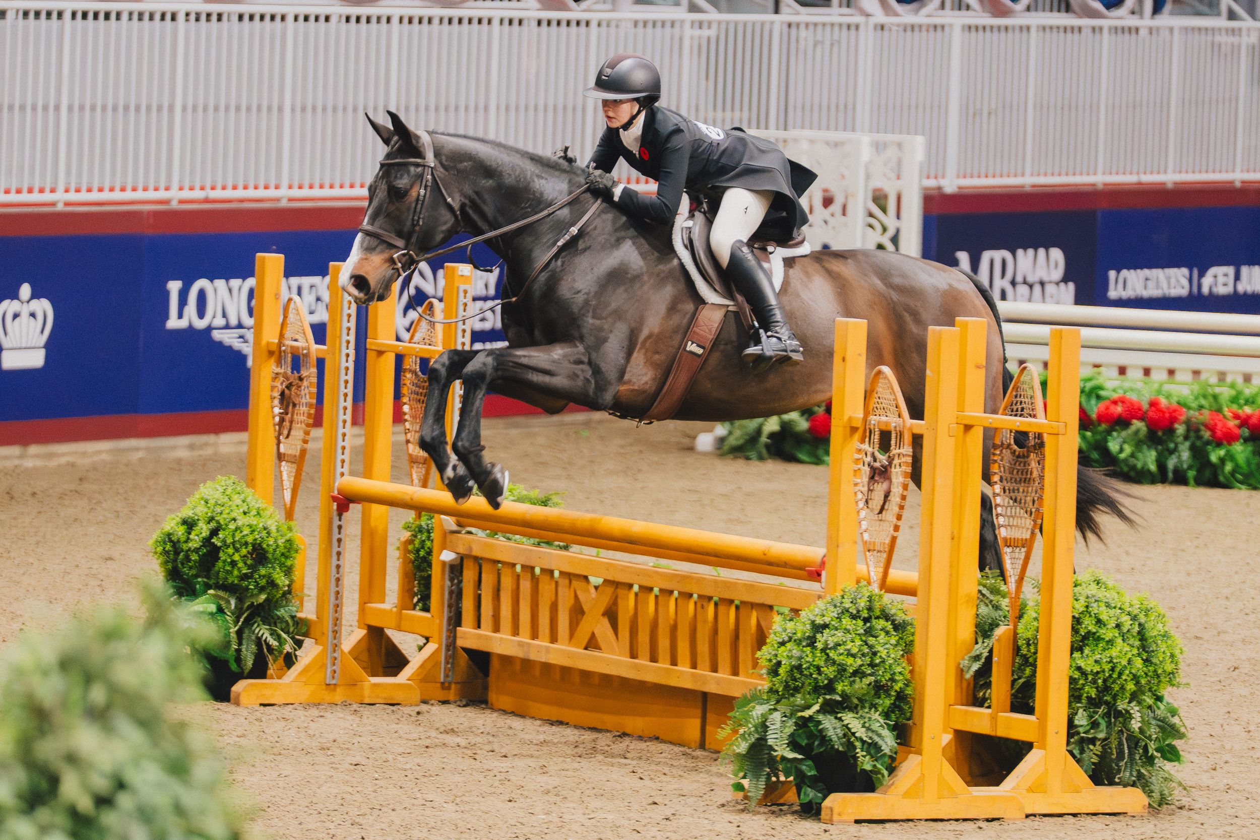 Horse and rider clearing a yellow and white jump obstacle during an equestrian competition.
