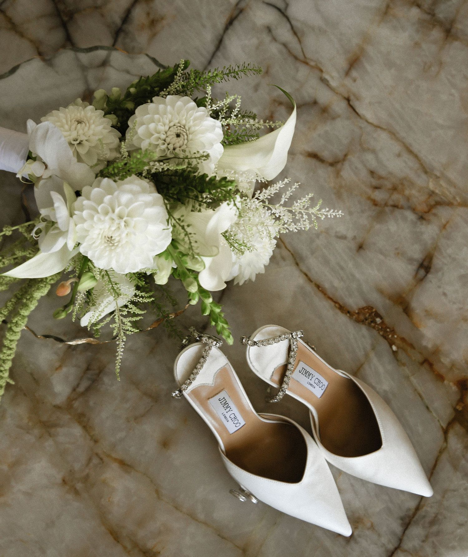 White wedding shoes with delicate floral arrangements featuring hydrangeas and greenery on marble surface.