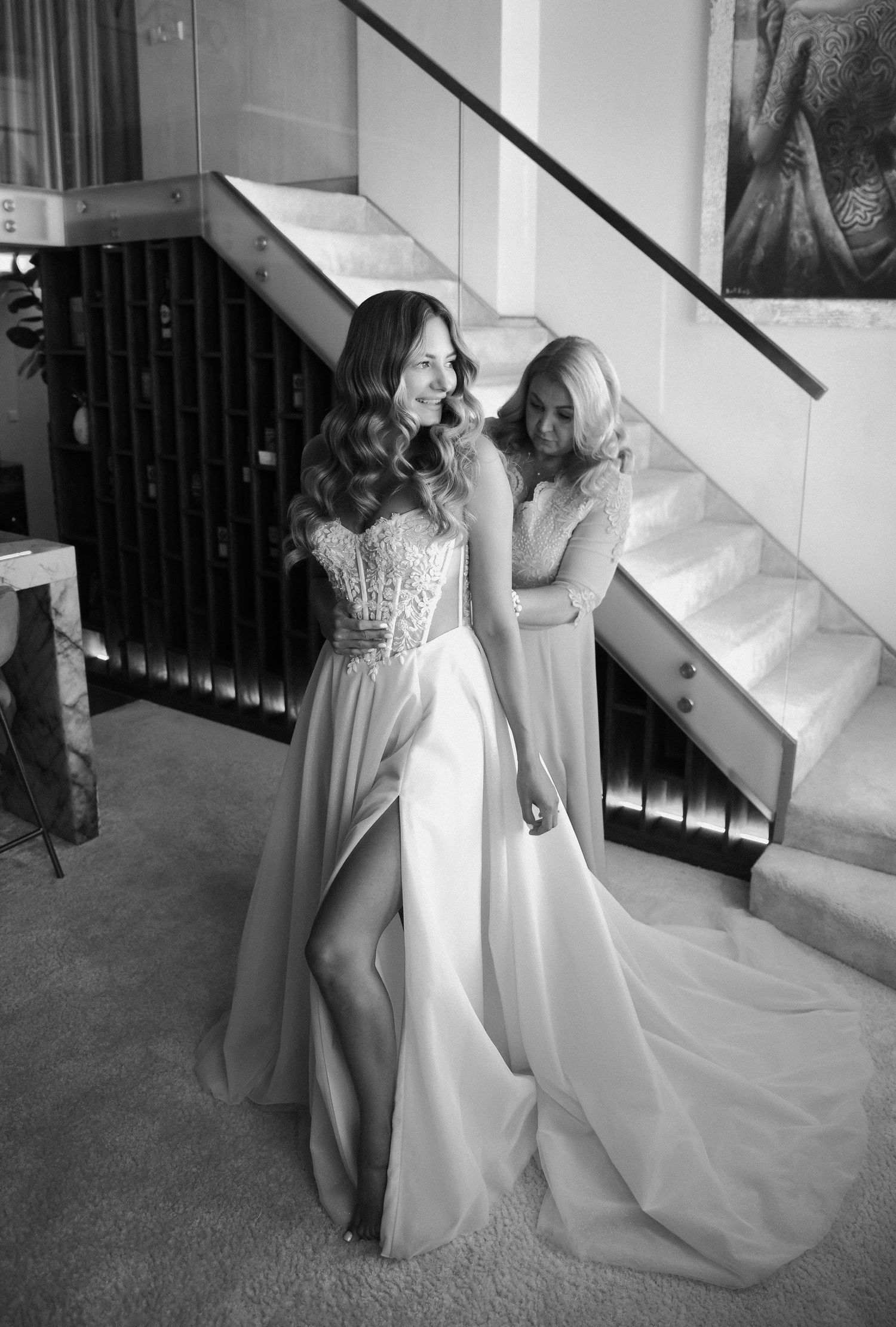 Black and white photo showing bridesmaids in elegant dresses gathered near a staircase.