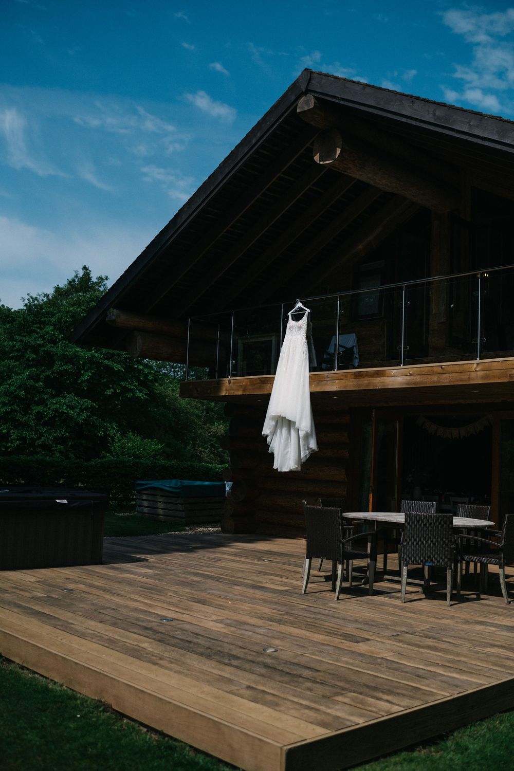 White wedding dress hanging on rustic wooden deck with blue sky backdrop.