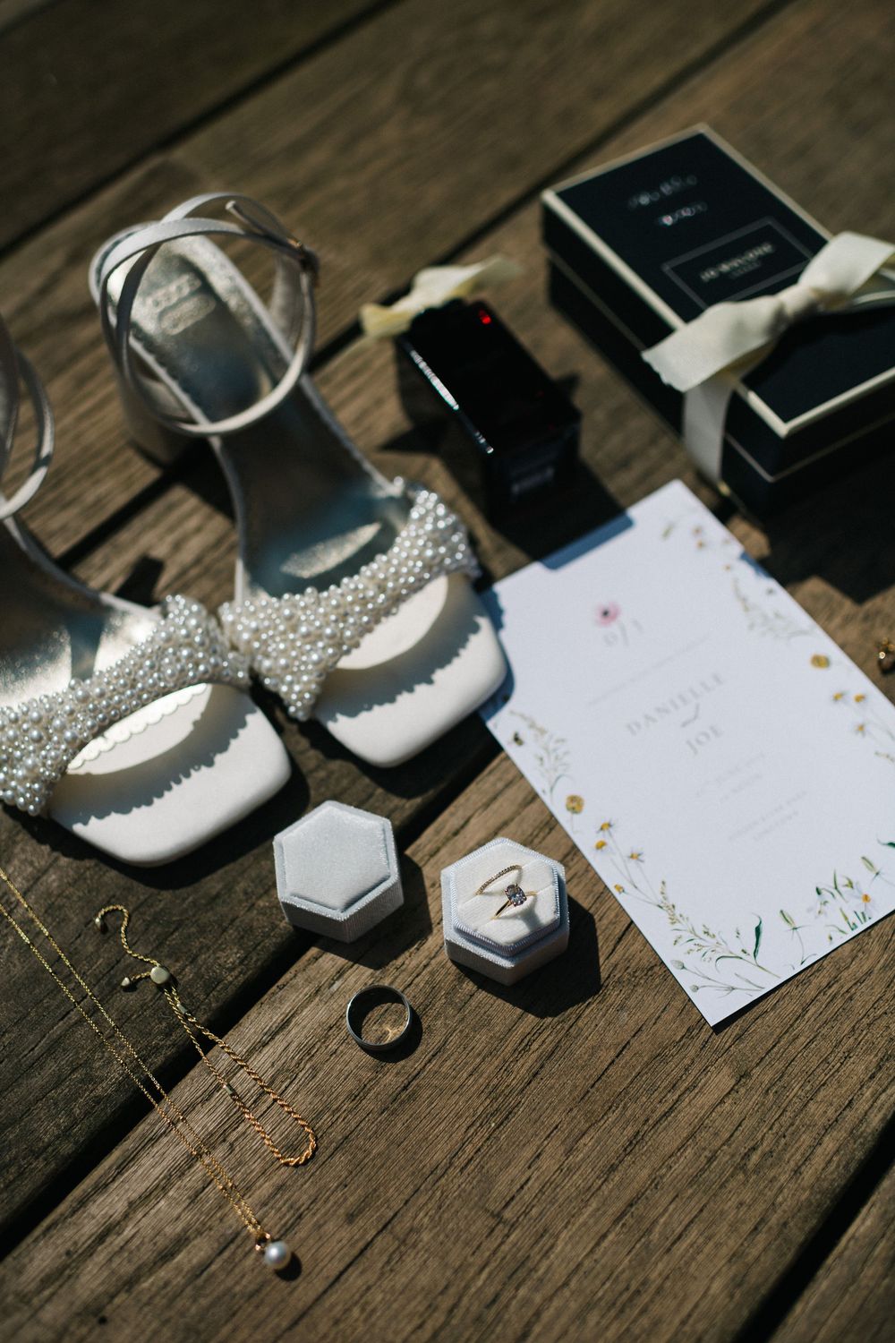 Wedding accessories and jewelry arranged on weathered wooden surface with invitation cards.