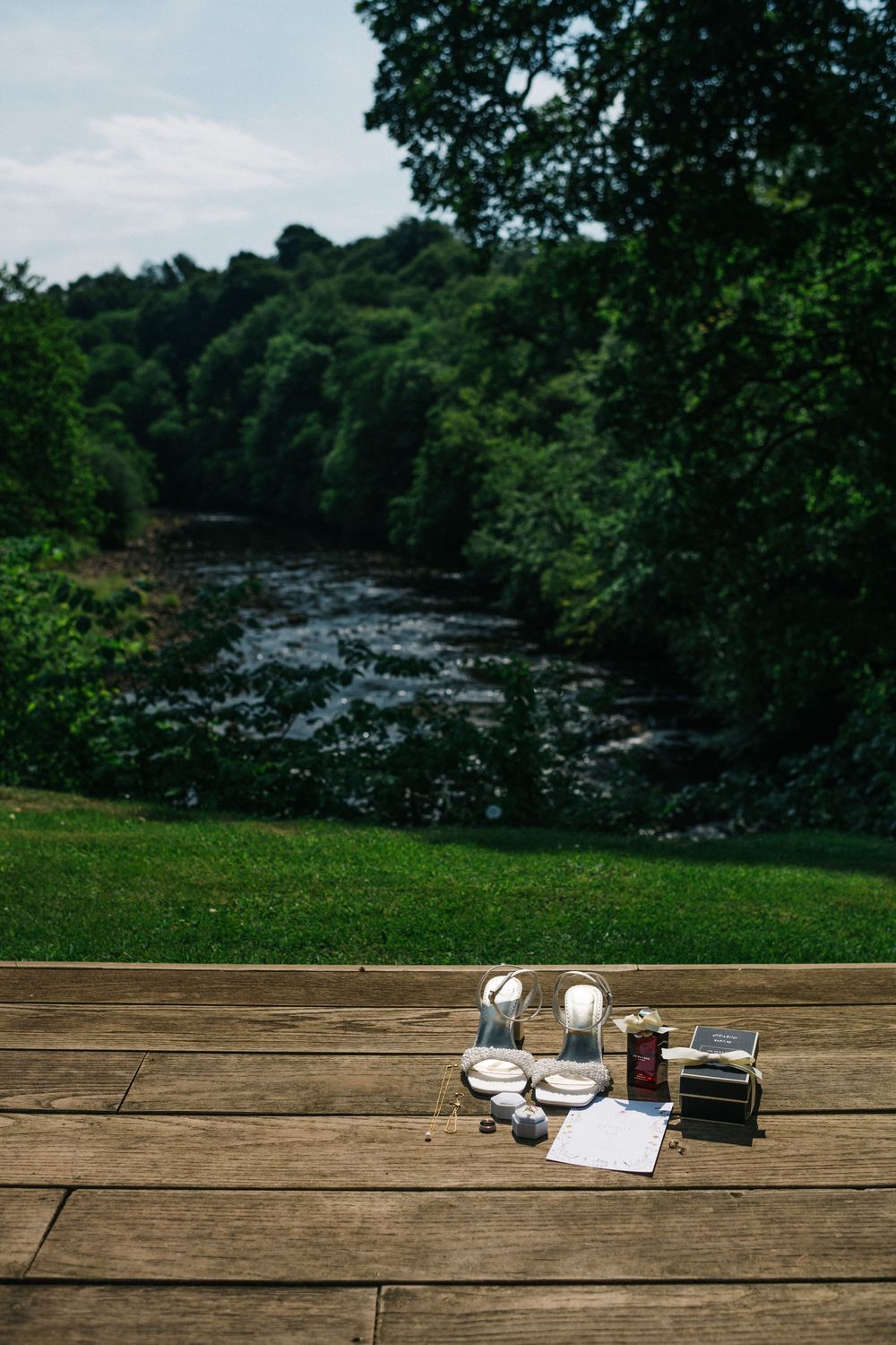 Scenic riverside view with wine glasses and papers on wooden deck overlooking lush forest.