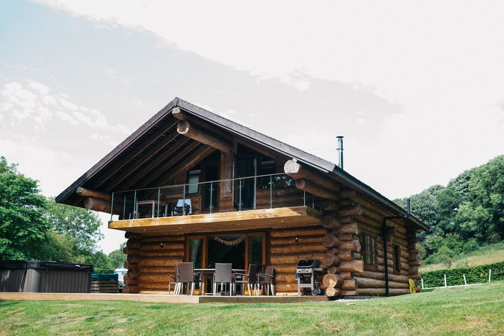 Modern log cabin with deck overlooking green mountain landscape.