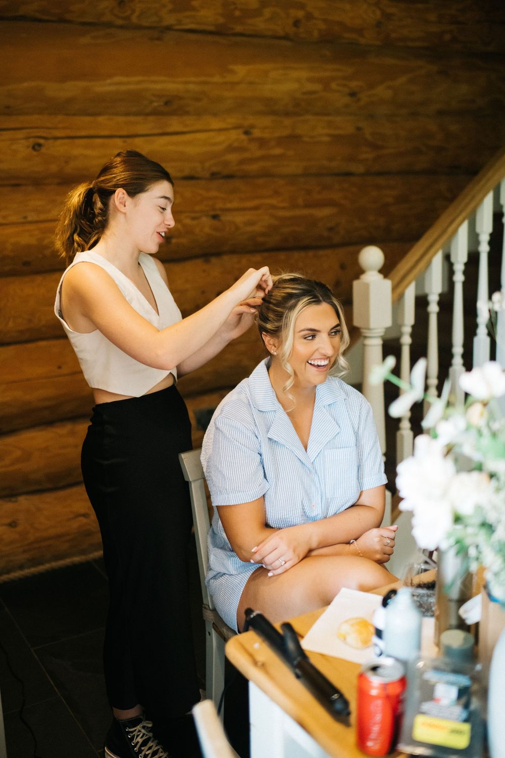 Wedding preparation scene in a rustic log cabin as final touches are being done to the bride's hair.