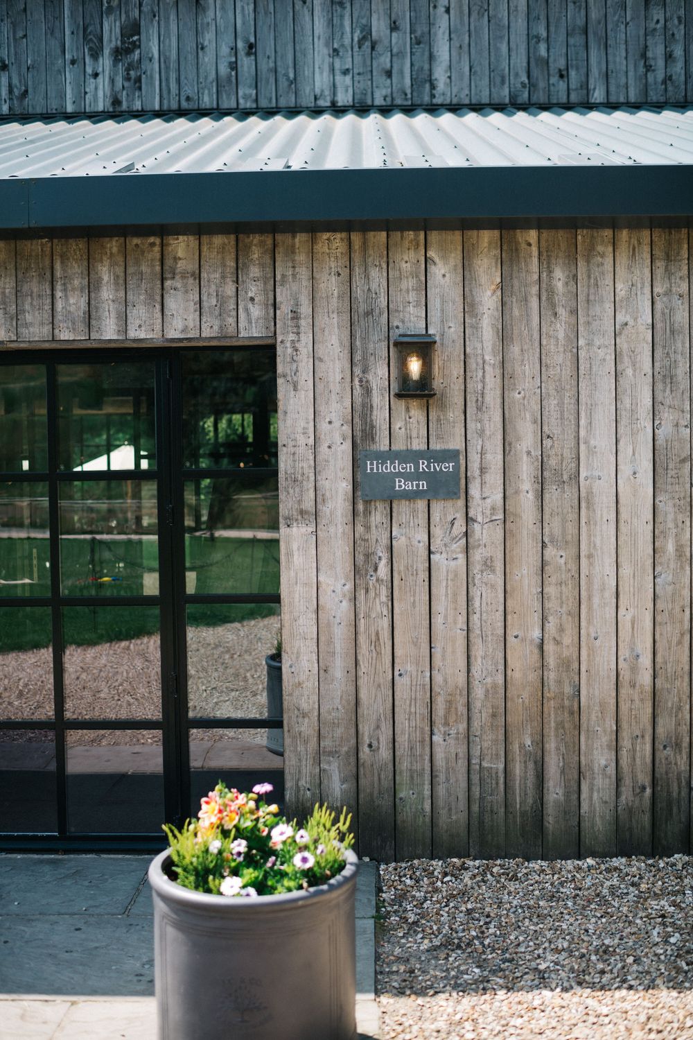 Rustic wooden exterior of Hidden Room venue with glass door and potted flowers.