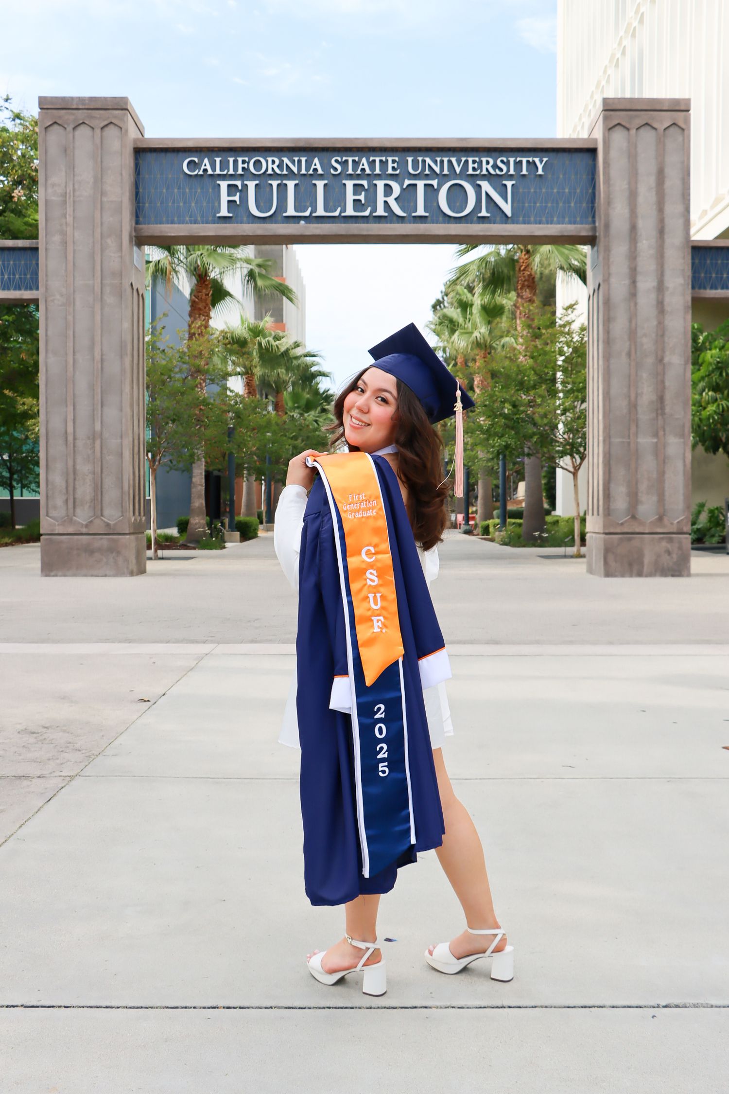 Graduate poses at Cal State Fullerton entrance wearing blue graduation stole and cap.