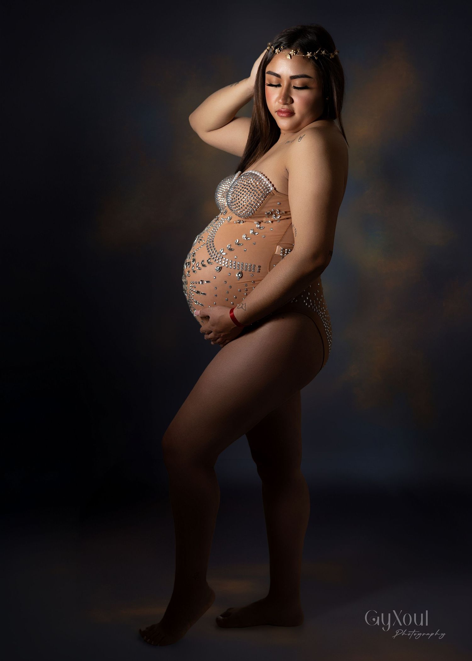 Artistic maternity photoshoot featuring an elegant beaded dress in a dark studio setting with dramatic lighting.