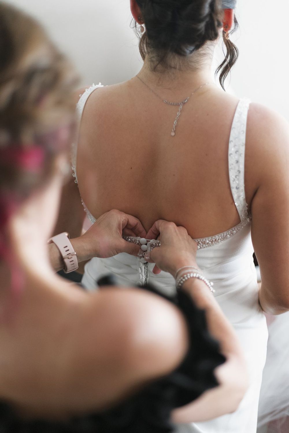 Bridesmaid fastening buttons on back of white wedding dress.