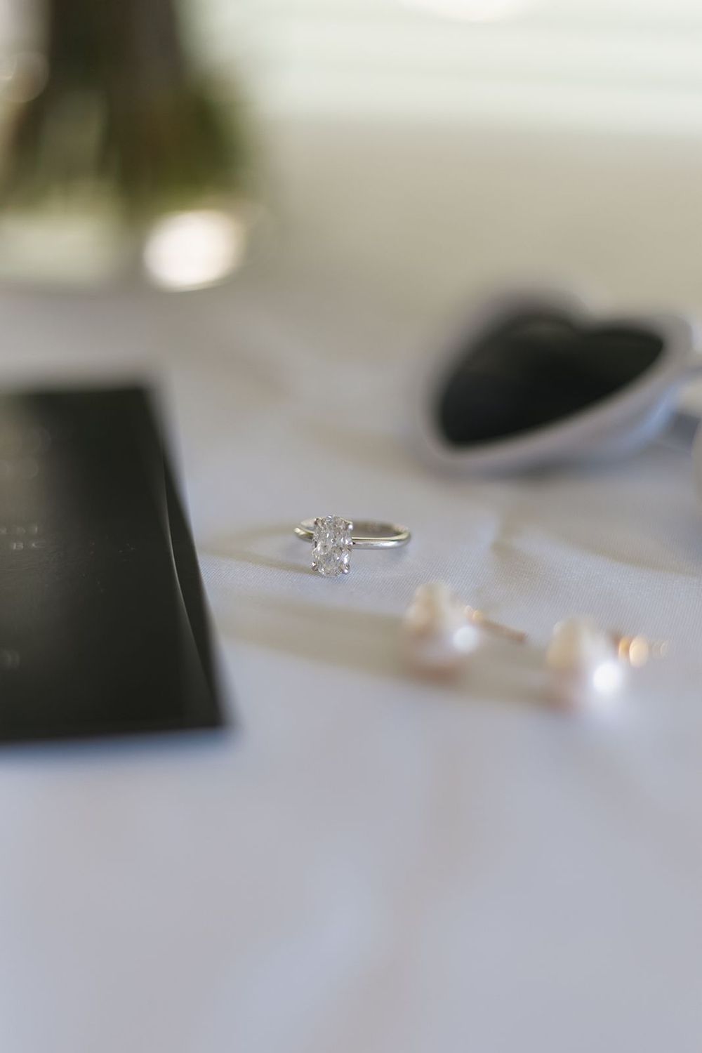 Diamond engagement ring and pearl earrings on white surface.