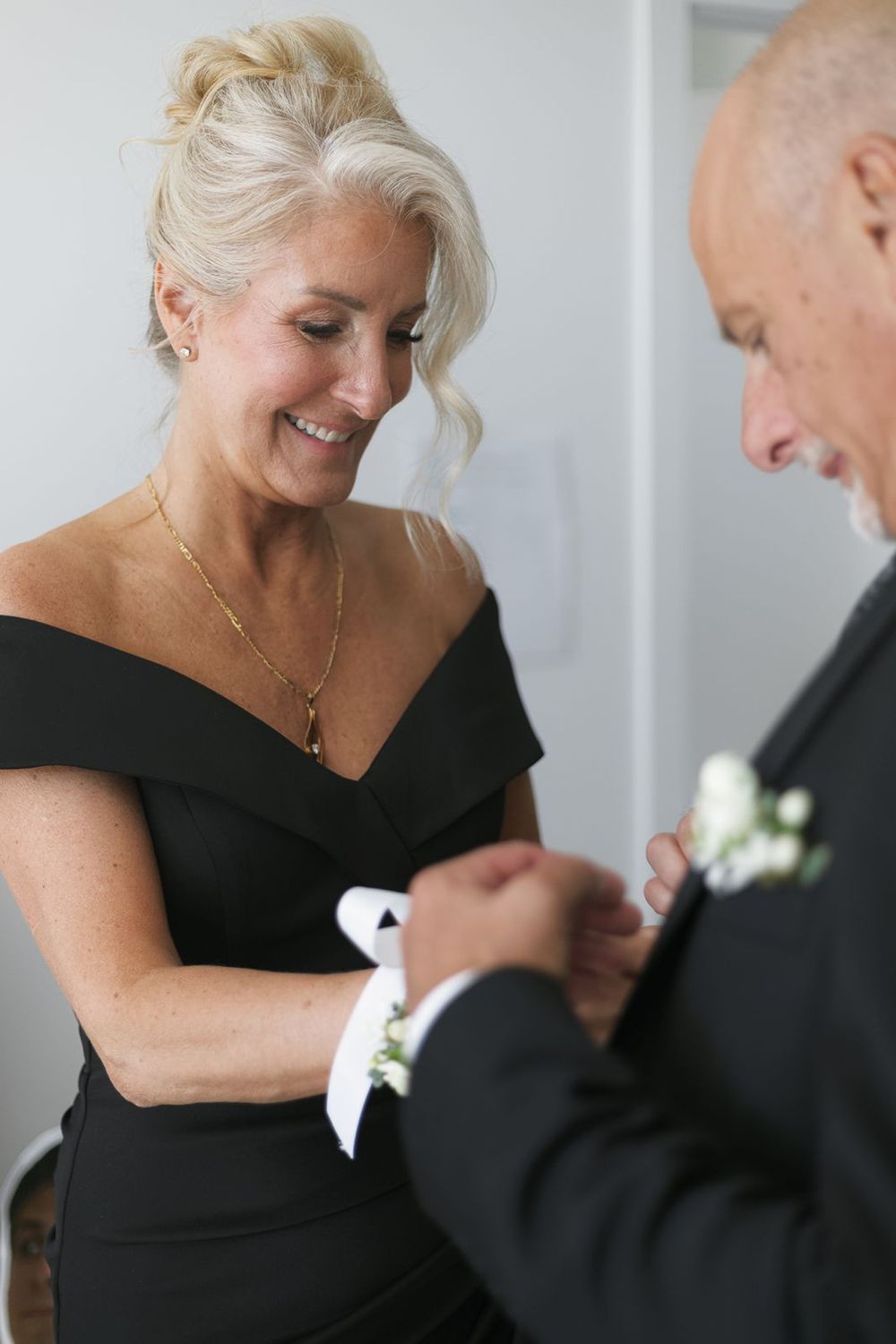 Smiling woman in black dress pinning boutonniere on mans lapel.
