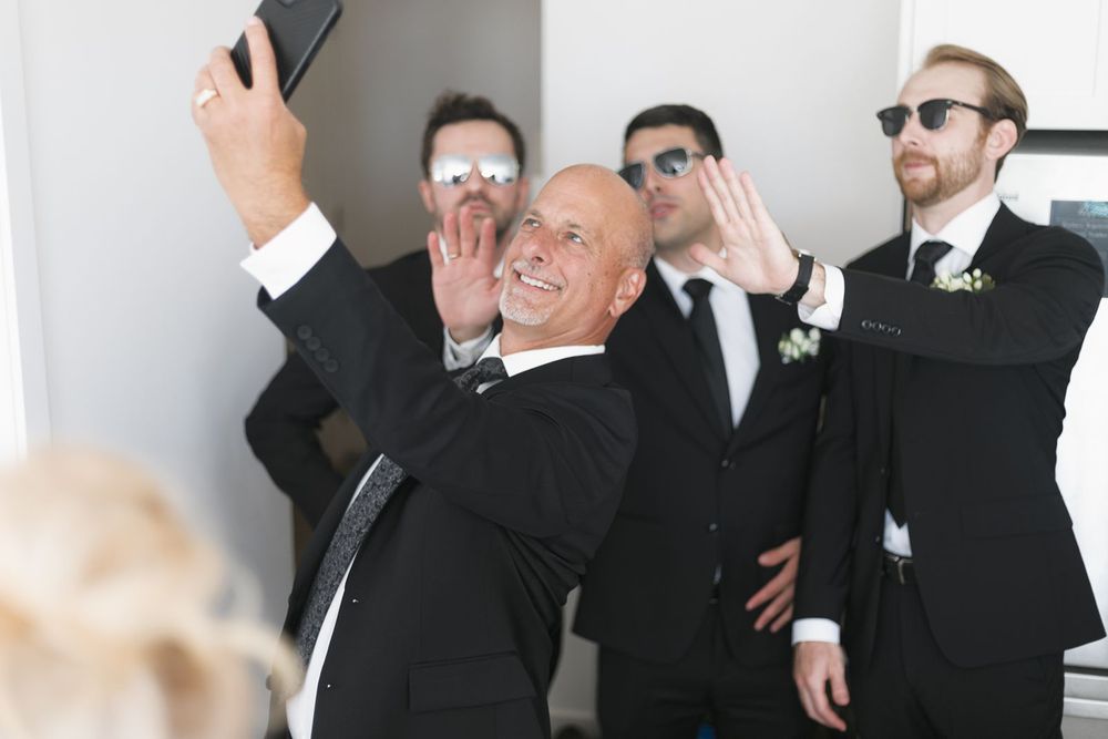 Groomsmen in black suits taking a fun selfie together.