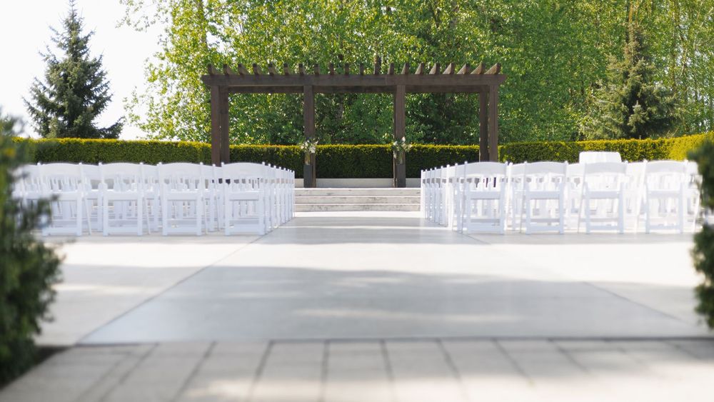 Elegant outdoor wedding venue with white folding chairs and wooden pergola altar on patio.