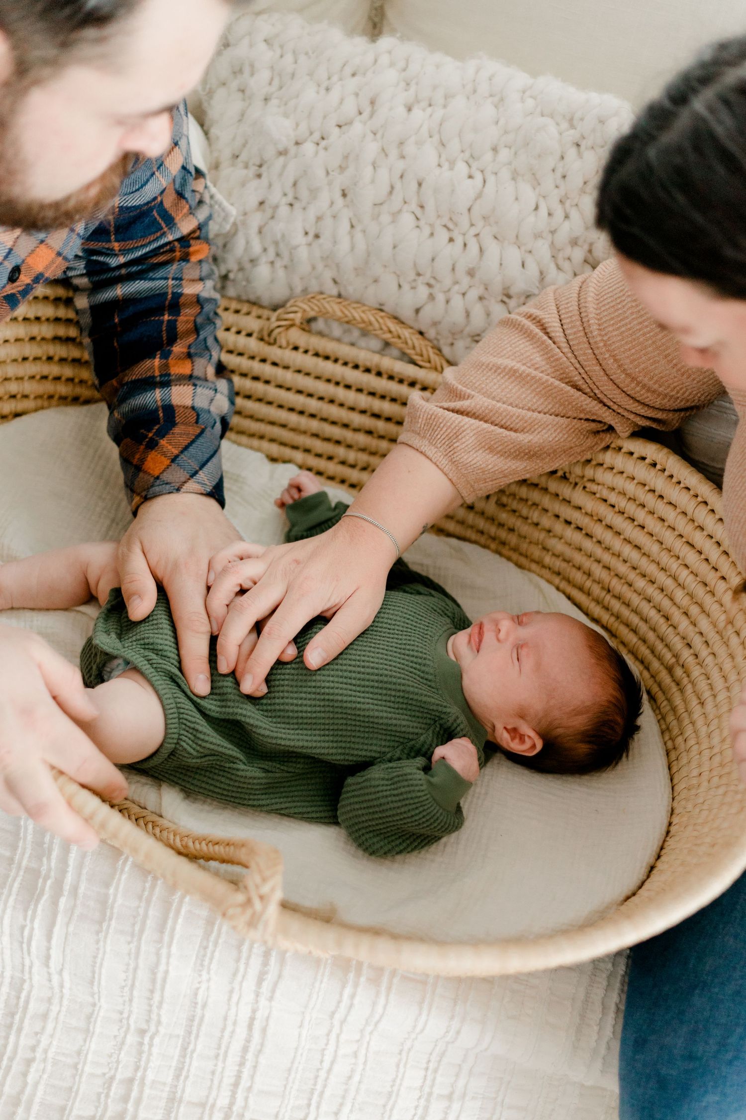 Parents tenderly watching over their newborn baby dressed in green in a woven Moses basket.