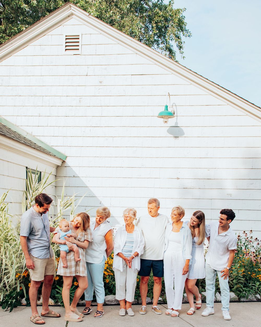 A line of people in white outfits pose against a white building wall.