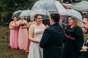 Wedding ceremony guests standing under clear umbrellas during an outdoor rainy celebration.