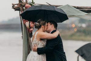 Romantic rainy day wedding photos of a couple sharing intimate moments under black umbrellas.