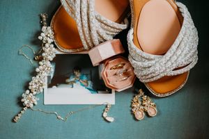 Wedding accessories including jewelry, shoes, and invitations arranged on a dark surface.