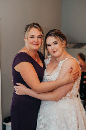 Two people embracing while wearing a white wedding dress and navy blue dress.