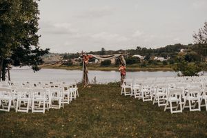 White folding chairs set up on a grassy field for an outdoor wedding ceremony with water views in the background.