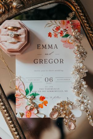 Floral wedding invitation for Emma and Gregor with delicate jewelry details in an ornate frame.