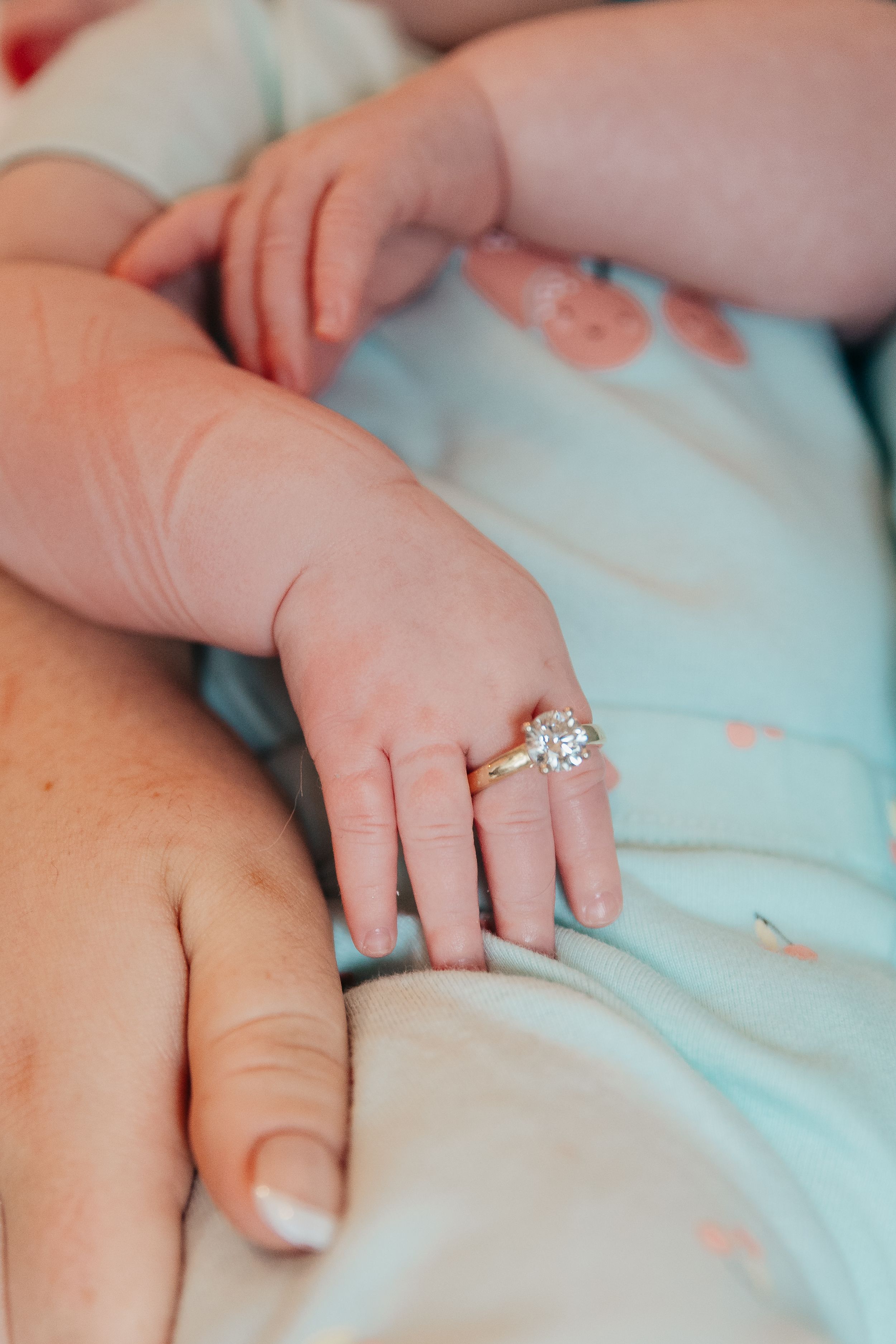 Close-up of hands wearing engagement ring and wedding band against light blue fabric.