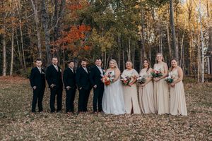 Wedding party poses in autumn forest with fallen leaves and golden sunlight filtering through trees.