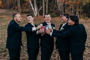 A group of people in black suits and formalwear raise glasses together in a celebratory toast during an autumn outdoor event.