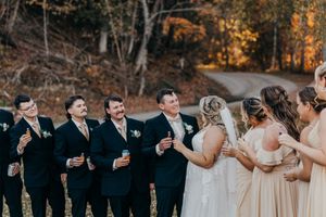 Wedding party in formal attire laughs together during outdoor autumn photo session.
