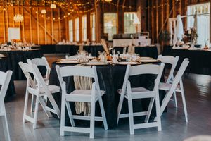 White folding chairs line up in rows inside an elegant barn venue decorated with warm string lights for a wedding.