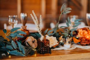 Rustic wedding table decor with eucalyptus leaves, candles, and warm lighting creating an intimate autumn atmosphere.