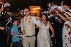 Wedding couple exits reception through sparkler send-off tunnel surrounded by celebrating guests at night.