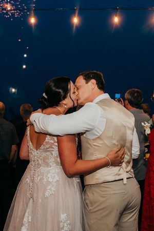 Wedding guests dance together in a circle on a dimly lit dance floor at an evening reception.