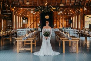 A rustic barn wedding venue with long wooden tables, string lights, and elegant table settings in warm ambient lighting.