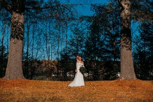 Wedding couple photographed walking through autumn trees with fallen orange leaves.