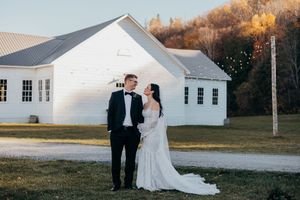 A couple poses in formal wedding attire in front of a white church building at sunset.