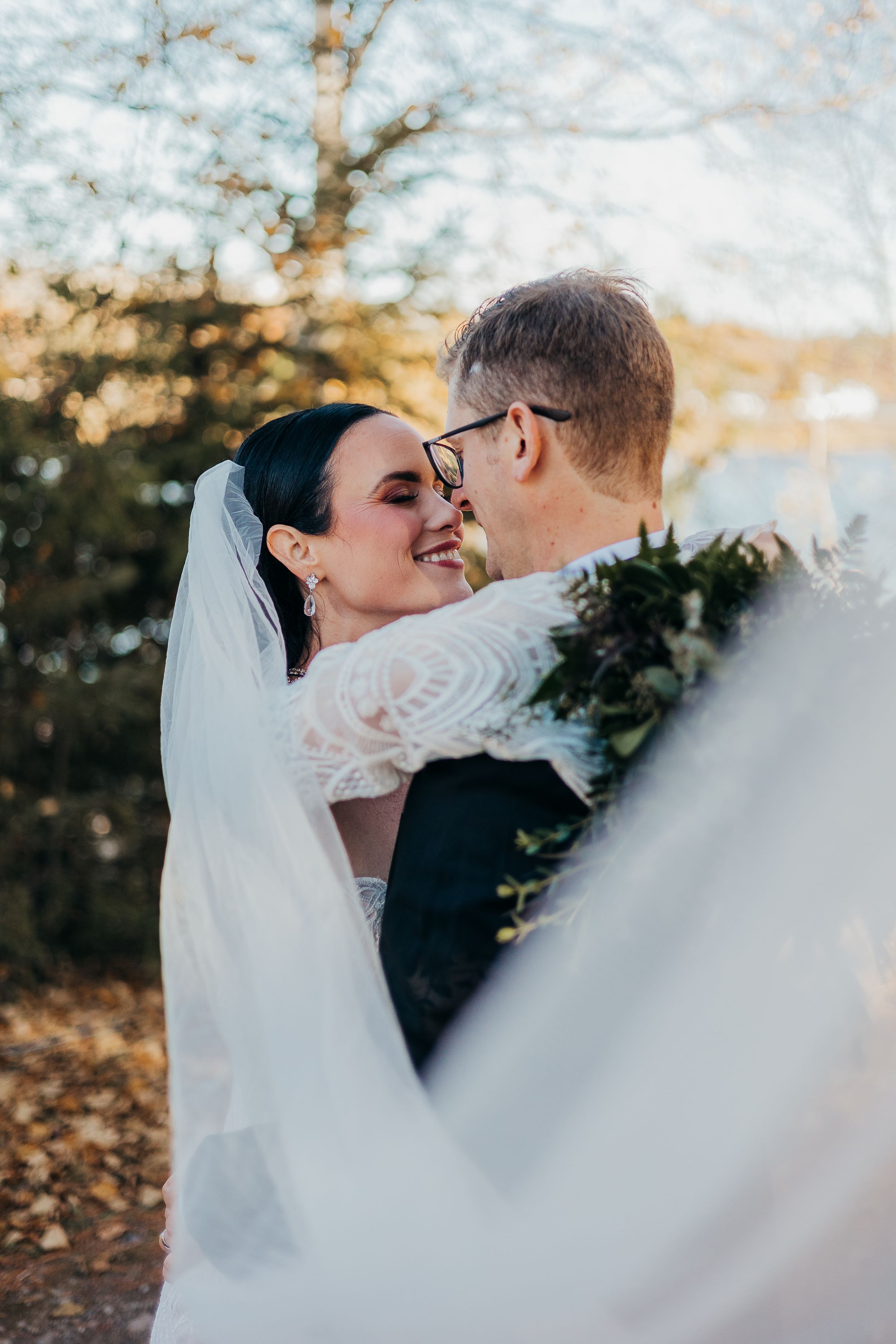 A romantic wedding moment captured outdoors during golden hour with a flowing white veil and floral bouquet.